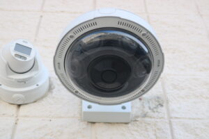 White dome security camera mounted on a beige tiled wall, close-up view of the lens housing.